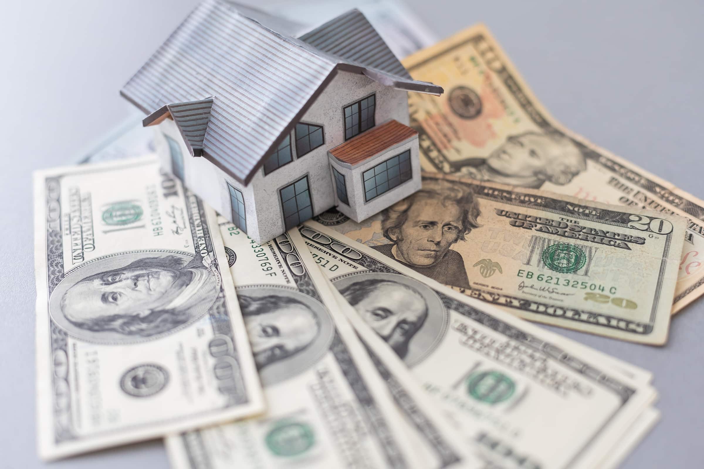 Model house sitting on top of a pile of cash