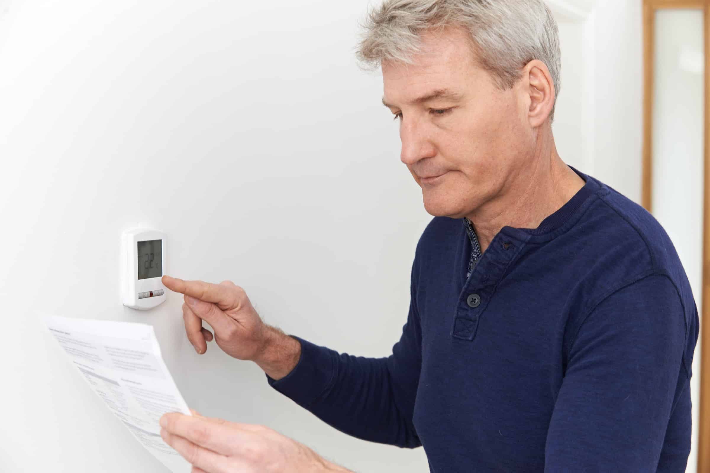 Worried looking man looking at energy bill while turning down the thermostat